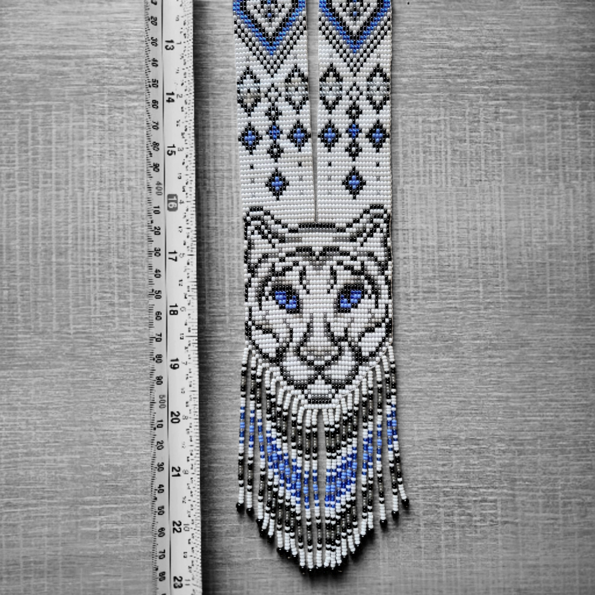 Tiger necklace flat lay beside a ruler showing loomed beadwork detail of the tiger face and fringe length