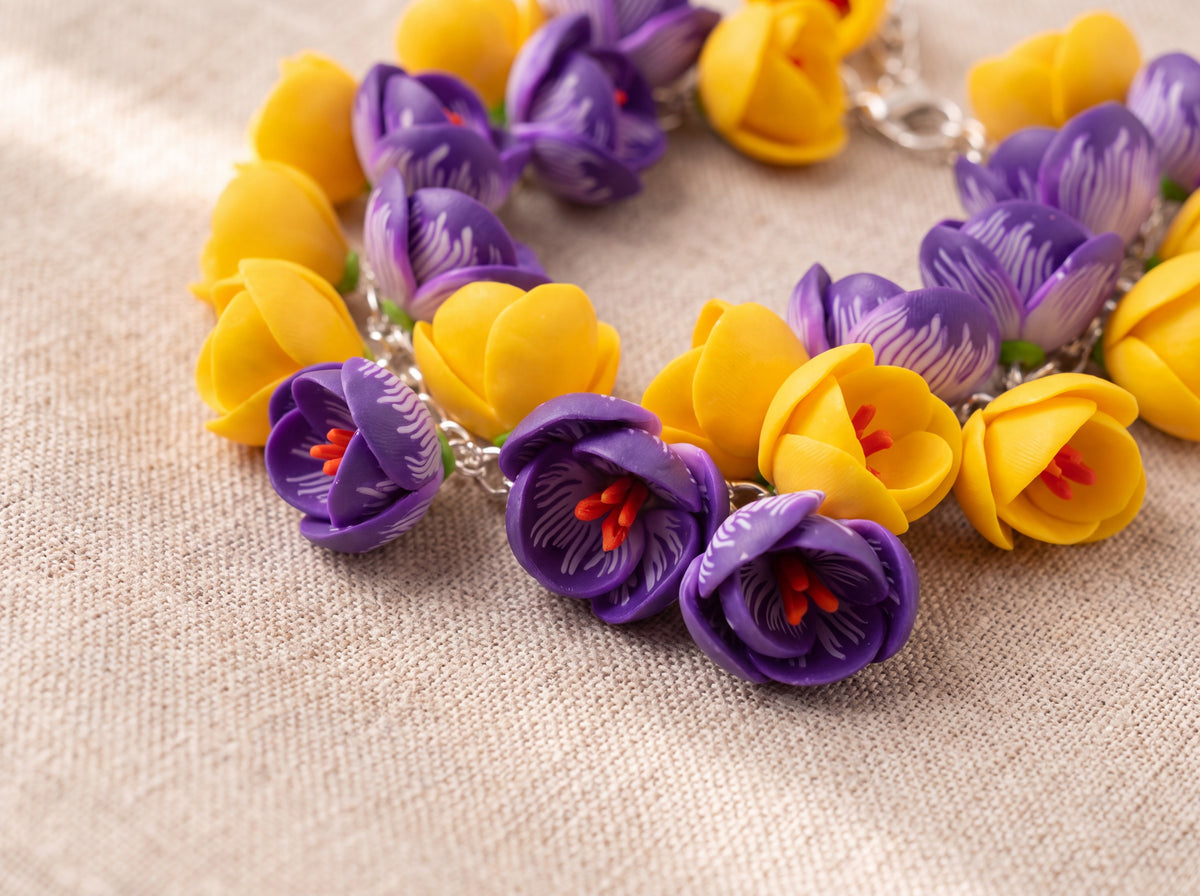 Close-up flat lay of a handmade flower bracelet with purple crocuses and yellow buds on a silver chain against beige linen.