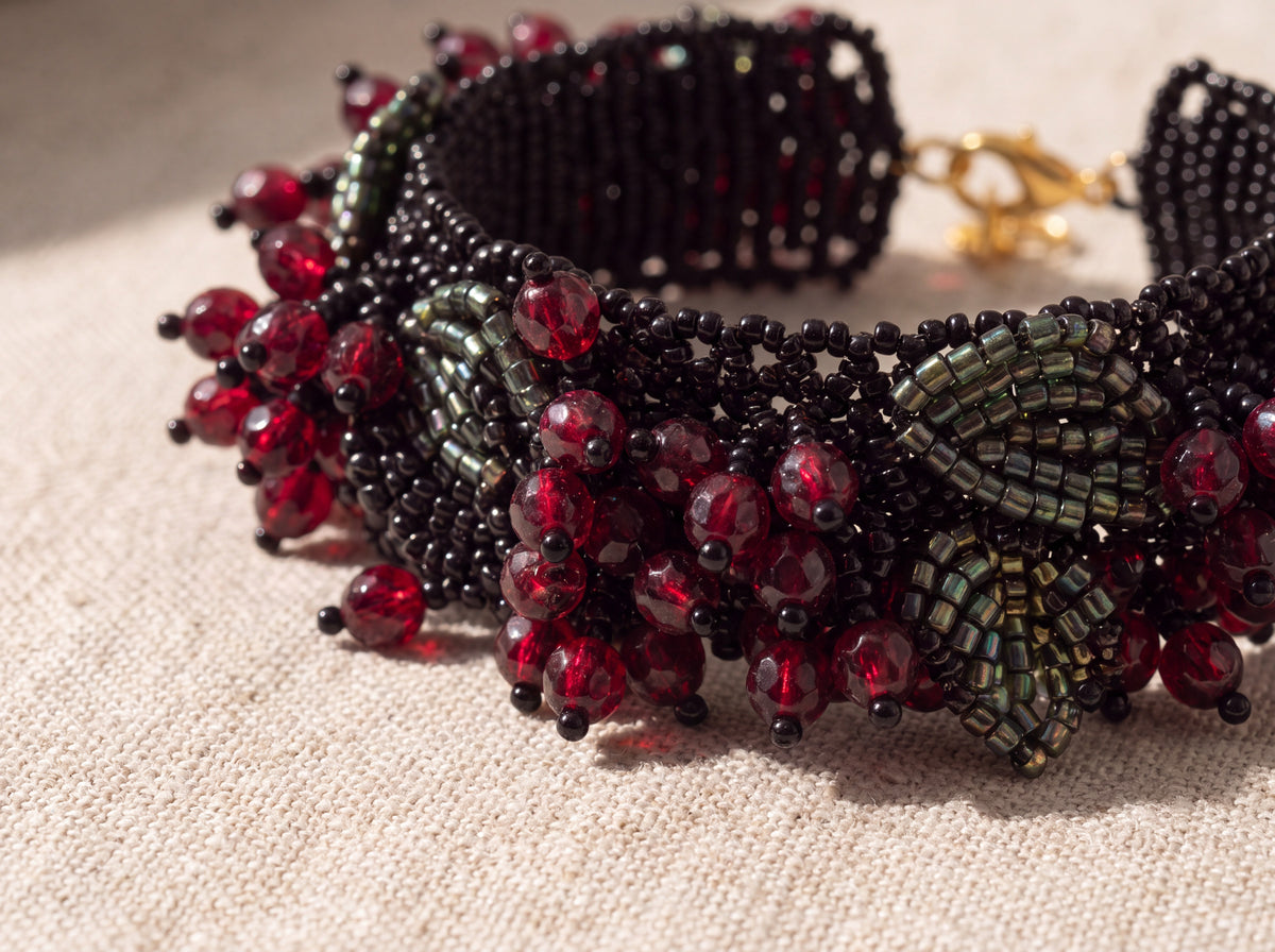 Macro detail of garnet-red glass berries and iridescent green beaded leaf on the black beaded cuff