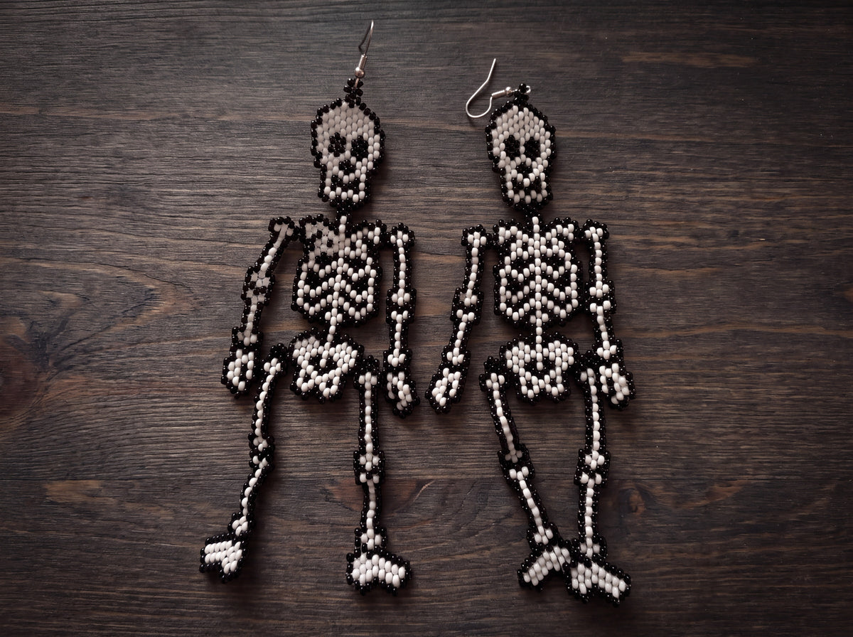 Pair of articulated beaded skeleton earrings laid flat side by side on dark wood