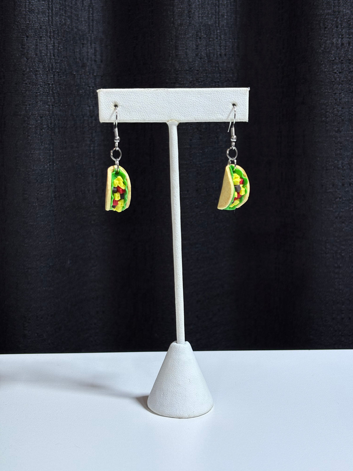Handmade taco earrings in polymer clay displayed on a white earring stand against a black backdrop