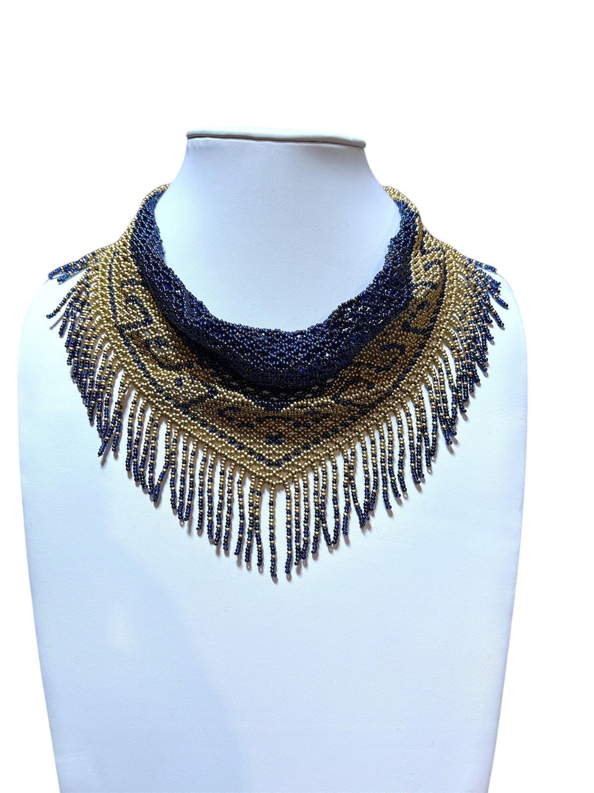 Navy blue and gold beaded scarf necklace draped loosely, showing ornament border and fringe, on a white bust