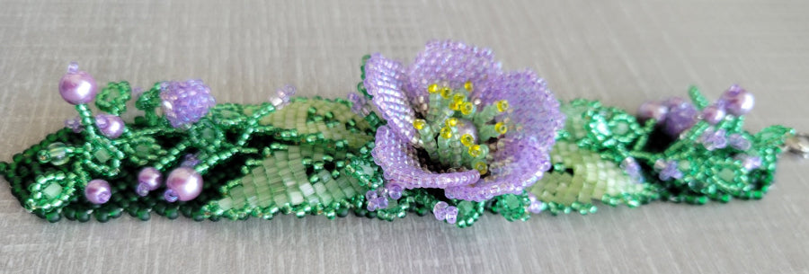 Beaded flower bracelet close-up in lavender purple with pearl buds and woven green seed bead leaves