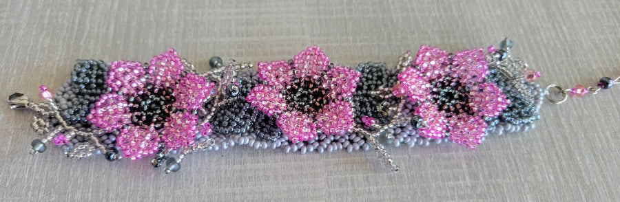 Flower bracelet colorway with pink beaded blossoms and gray leaves on a lilac seed bead band, flat lay