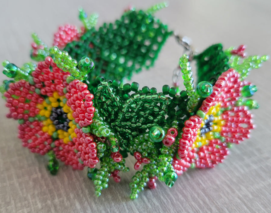 Beaded flower bracelet with red poppy blossoms and green leaves, angled view showing the silver clasp