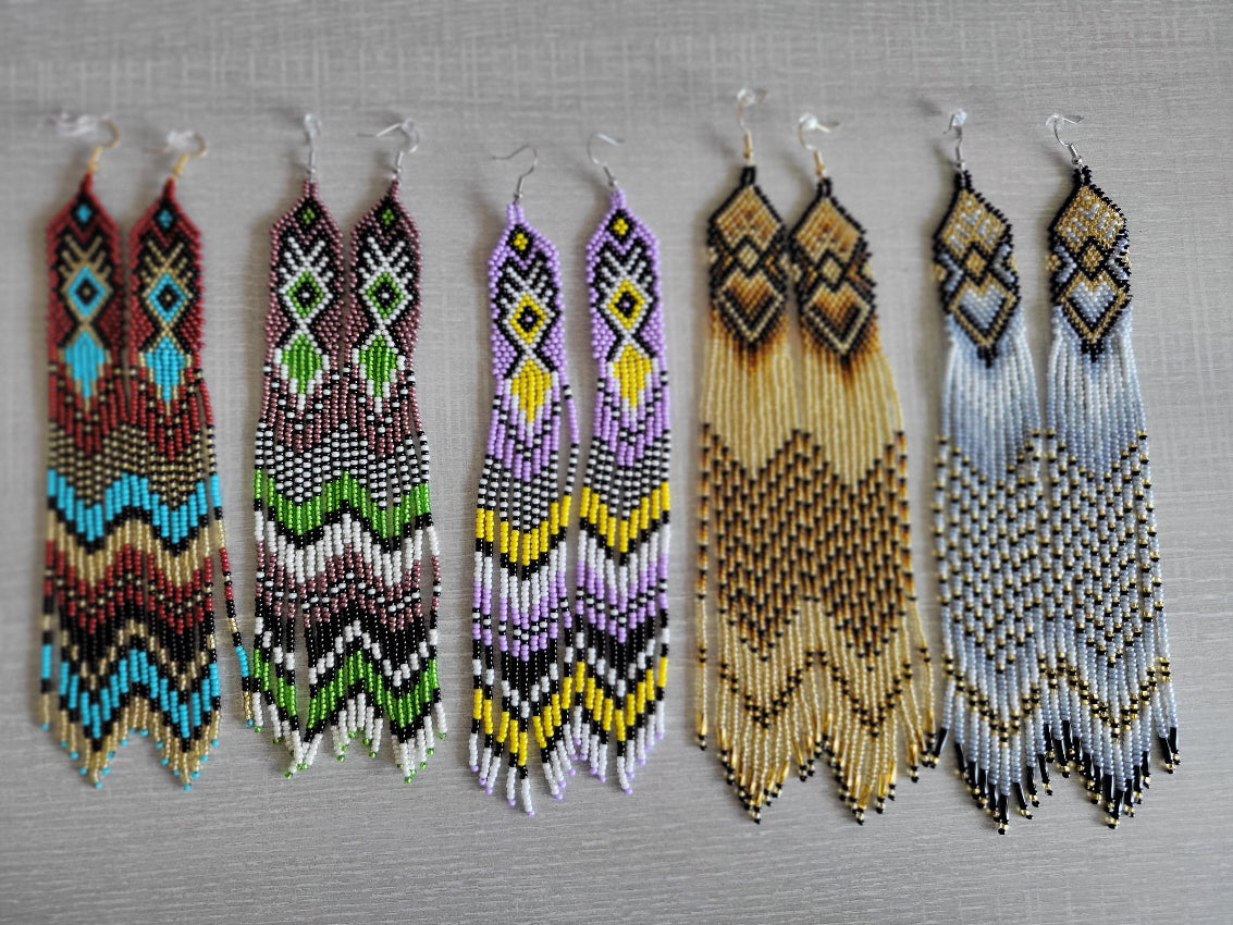 Five colorways of extra long handmade beaded fringe earrings arranged in a flat lay on gray background
