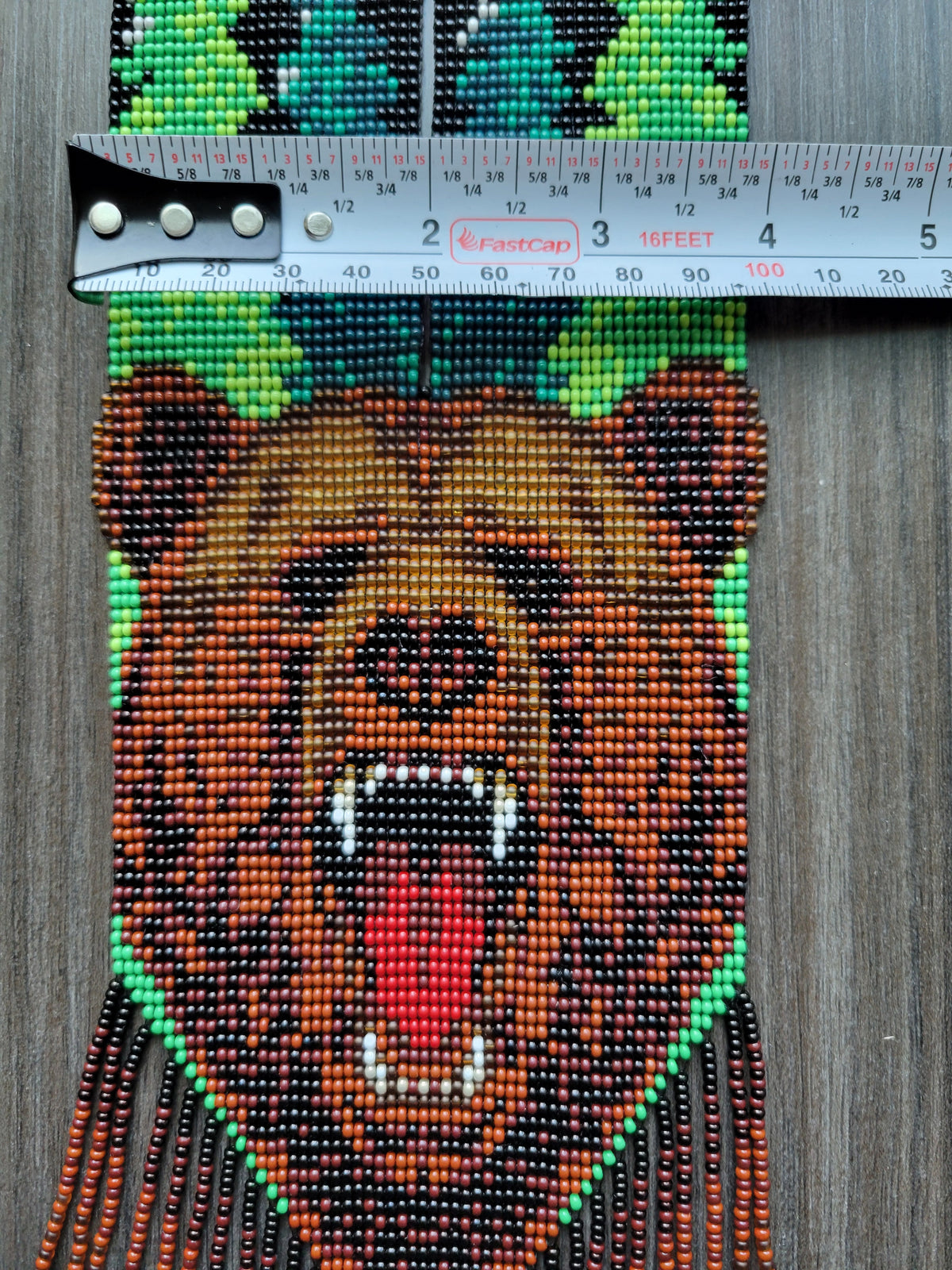 Close-up of the loomed bear face beadwork on the Bear gerdan XL with a tape measure showing its width