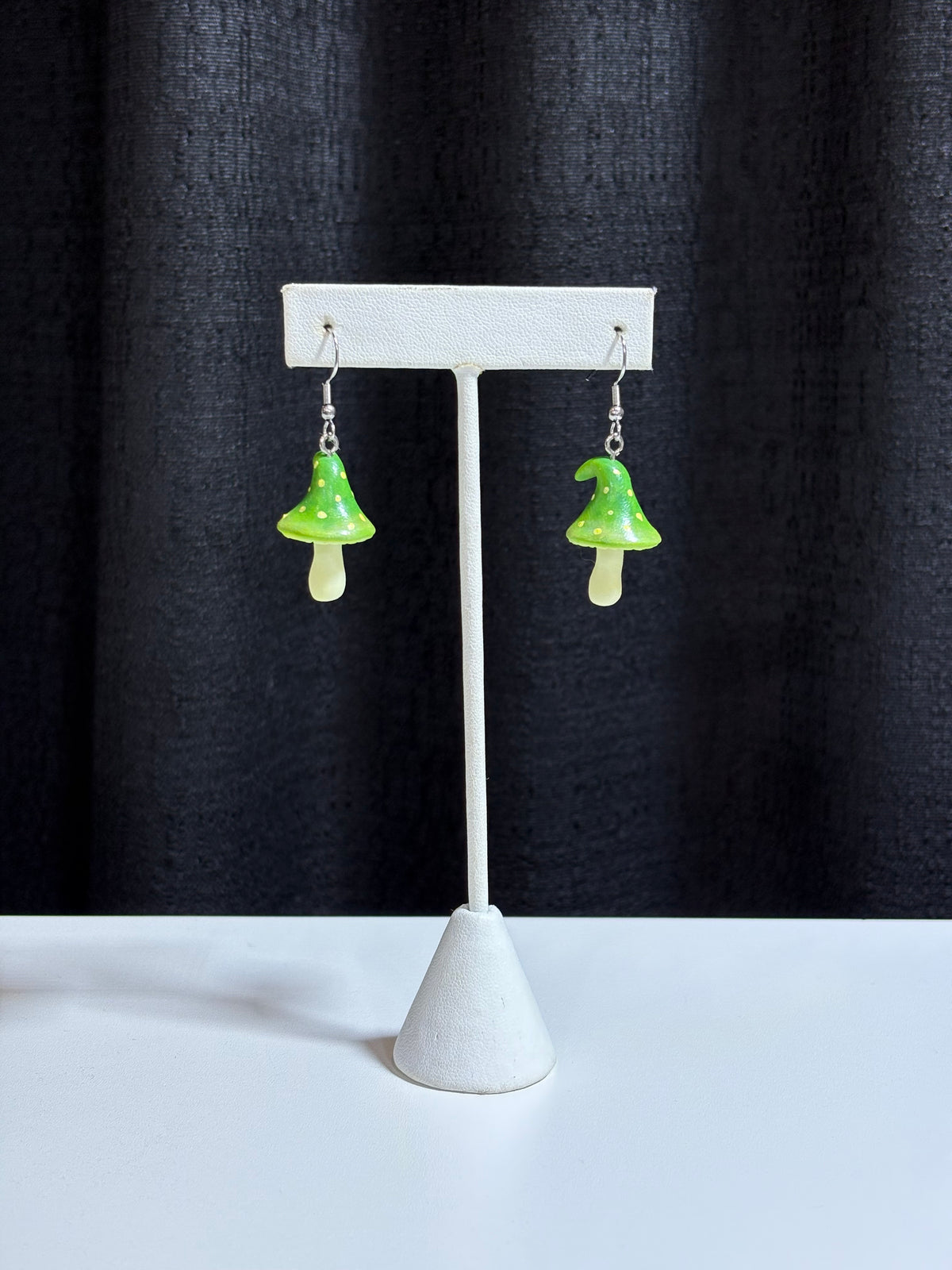 Polymer clay fairy mushroom earrings with green caps shown on a white display stand, black backdrop