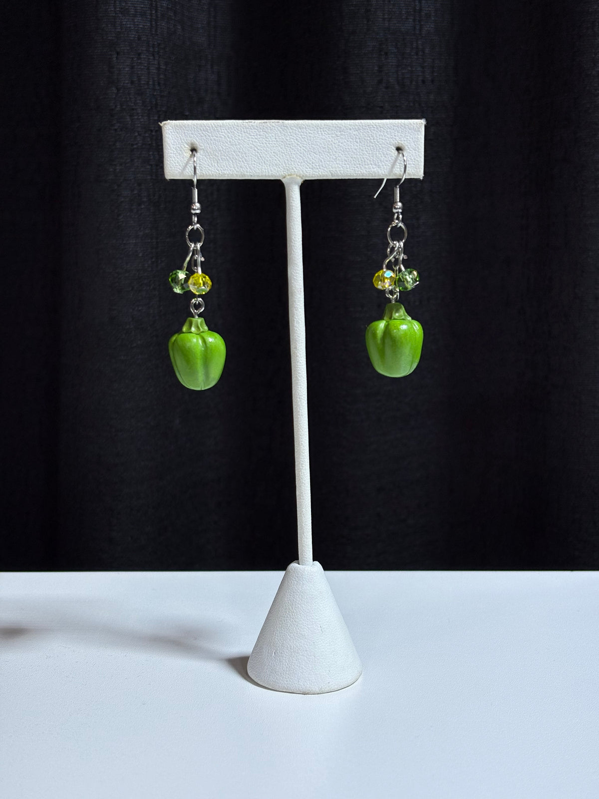 Green bell pepper dangle earrings with crystal accents displayed on a white stand, black backdrop