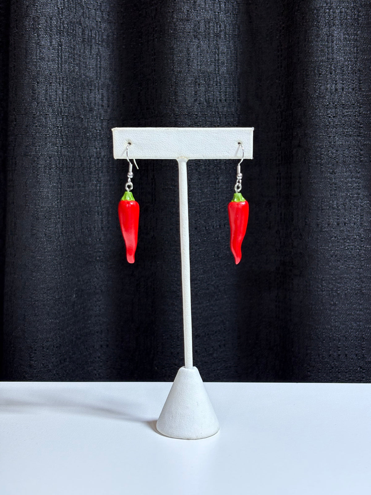 Handmade chili pepper dangle earrings on silver hooks, displayed against a black curtain backdrop
