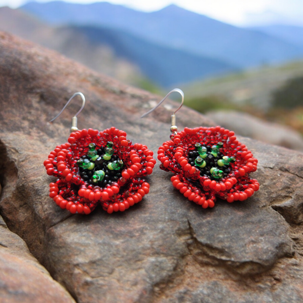 Beaded red poppy flower earrings resting on a rock with mountains in the background