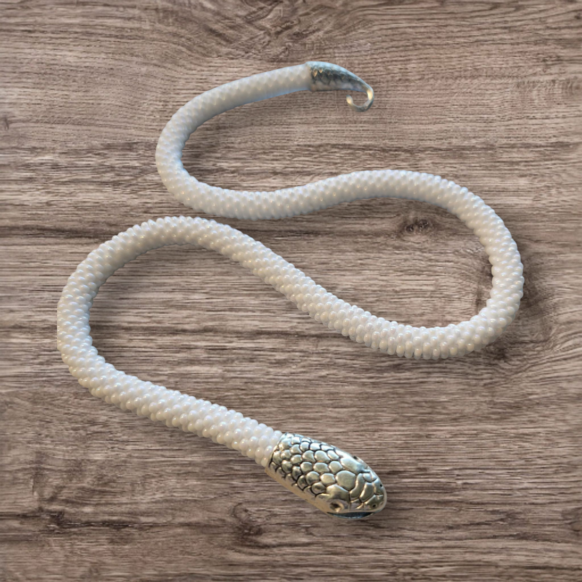 White crochet-beaded snake choker winding over weathered wood with silver scaled head and hook tail