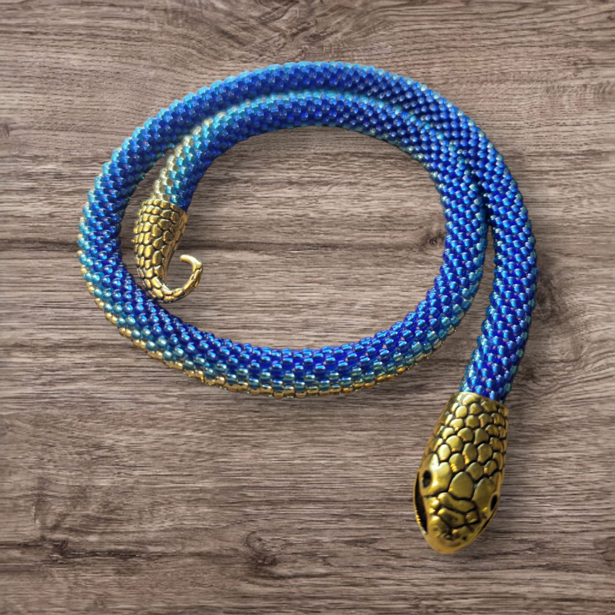 Royal blue and gold beaded snake choker coiled on rustic wood, brass snake head clasp, overhead view