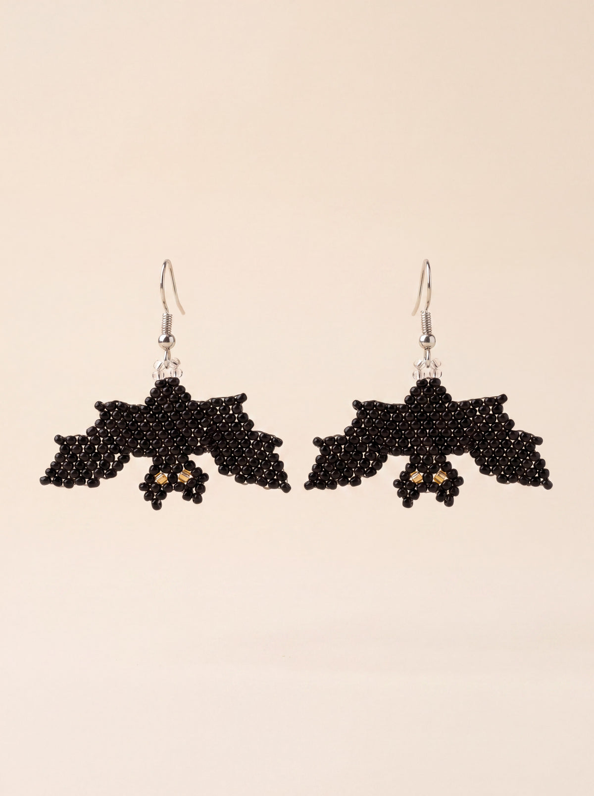 Handmade black beaded bat earrings with gold eyes hanging side by side on silver hooks, on cream