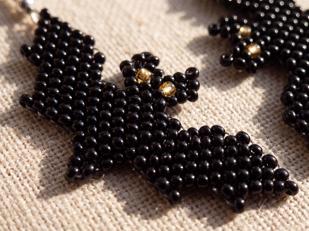 Macro detail of the beaded bat's head and wing showing the two gold eye beads, on oatmeal linen