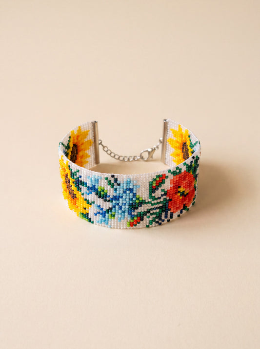 Handmade loomed beaded cuff bracelet with sunflower and poppy motifs on a white background, glass seed beads