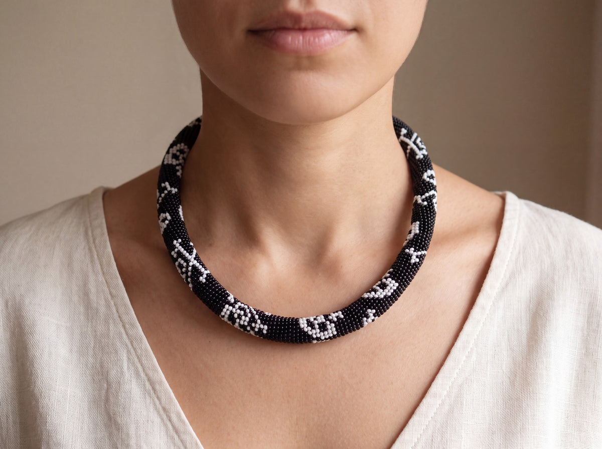 Handmade black bead-crochet rope necklace with white skull motifs worn on a model over a cream linen top