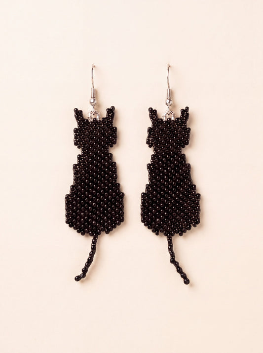 Handmade black beaded sitting cat silhouette earrings with beaded tails hanging side by side on silver hooks, on cream