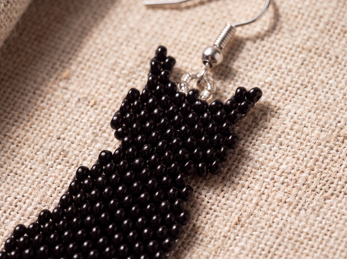 Macro detail of the glossy black beadwork and free-hanging beaded tail, on oatmeal linen