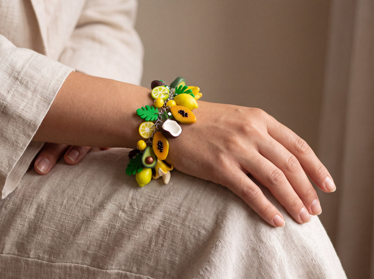 Handmade tropical fruit charm bracelet with polymer clay lemons, papayas, bananas, coconuts and monstera leaves, worn on a model's wrist
