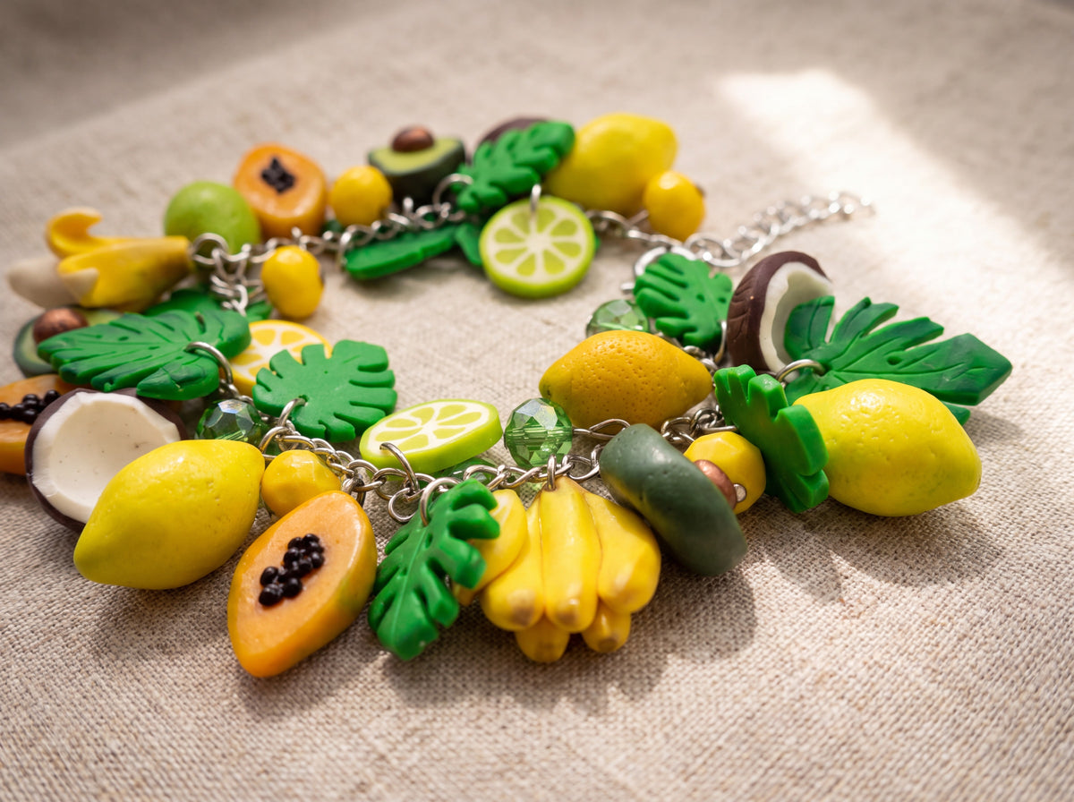 Close-up flat lay of a handmade charm bracelet with miniature tropical fruits - lemons, papaya, bananas, limes, coconut and green leaves - on linen