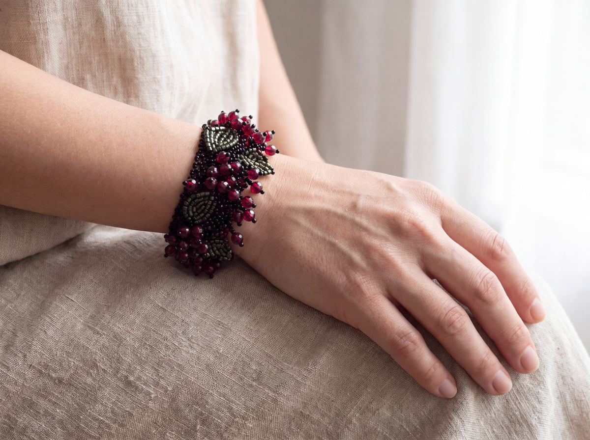Red berries beaded cuff worn on the wrist with a relaxed hand on linen