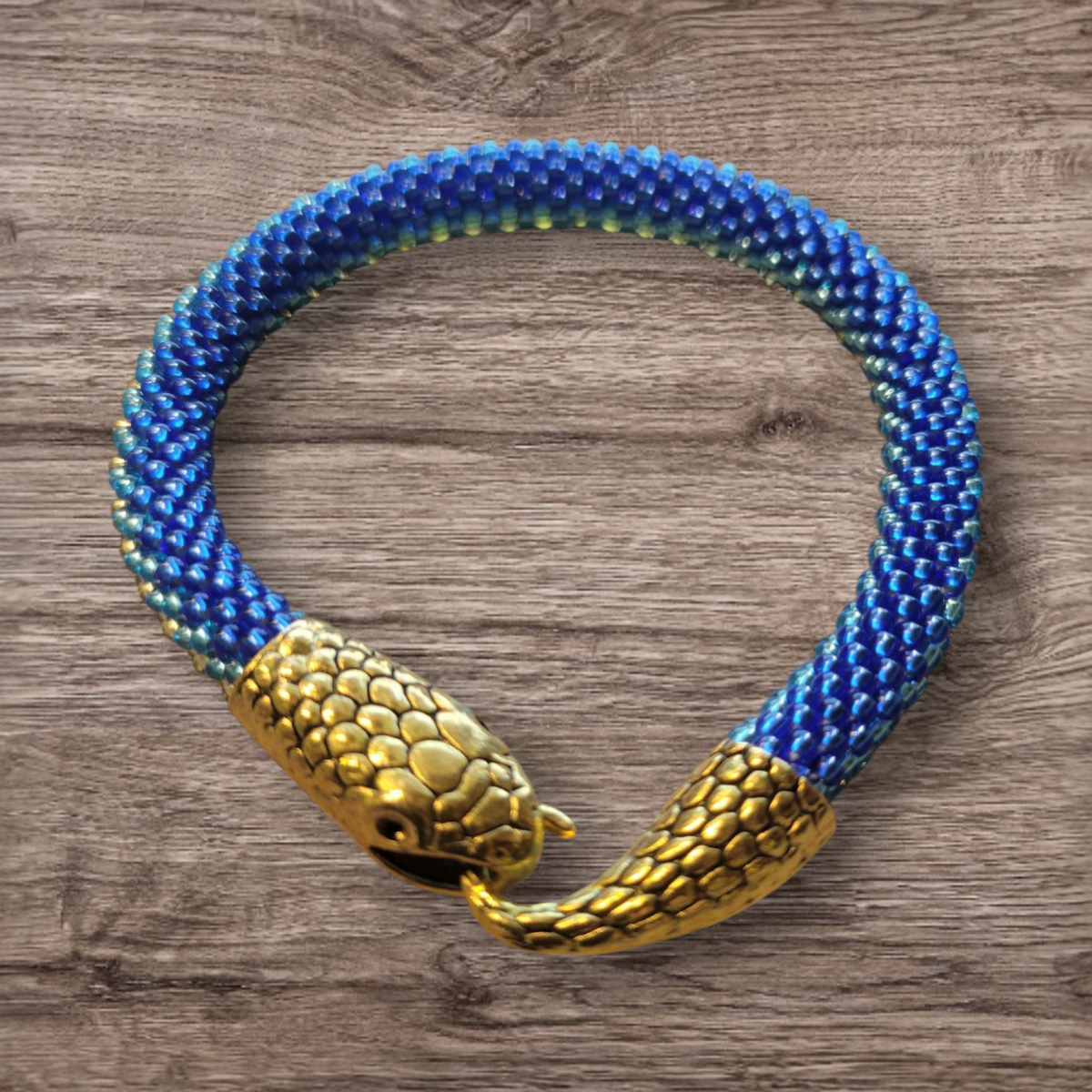 Beaded snake bracelet in cobalt blue and gold seed beads with gold serpent head clasp on a wood background