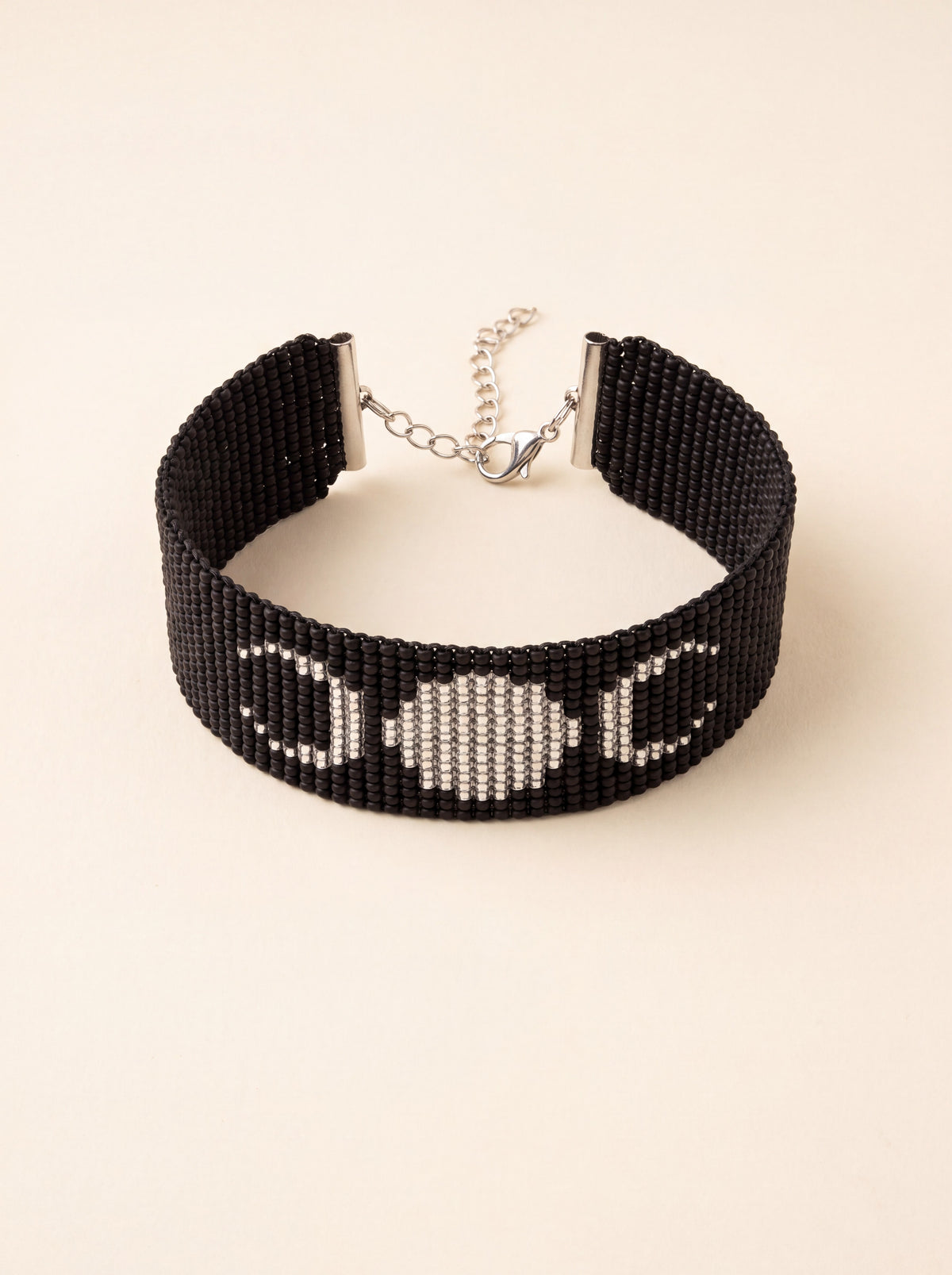 Handmade loom-beaded black bracelet with silver triple moon symbol, coiled flat on cream