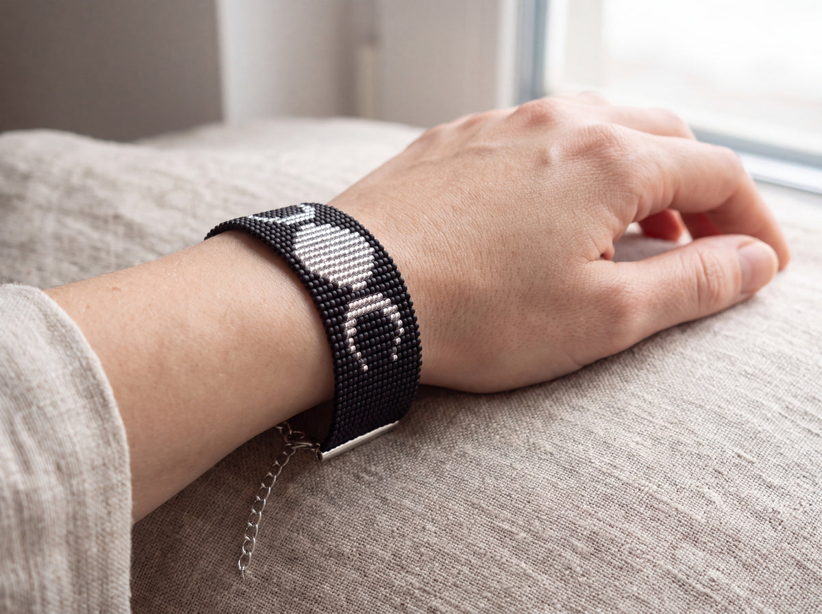 Black beaded triple moon bracelet worn on the wrist with a relaxed hand on linen
