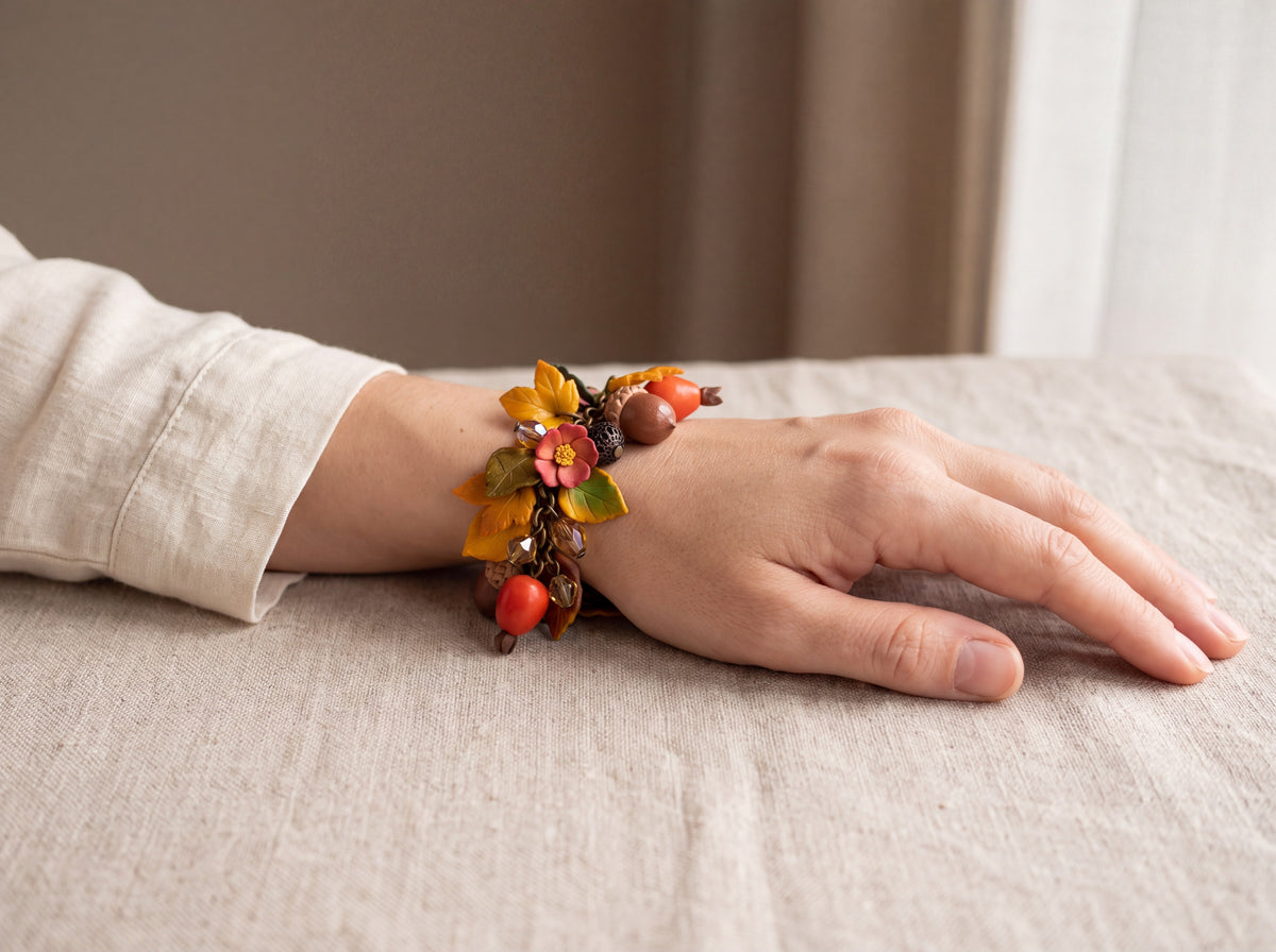 Handmade autumn charm bracelet with dog-rose hips, acorns, golden leaves and amber beads, worn on a woman's wrist.
