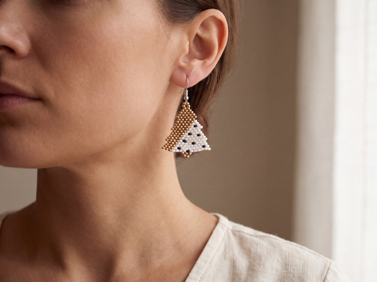 Handmade beaded Christmas tree earring in white with black dots and matte gold, worn on a model's ear