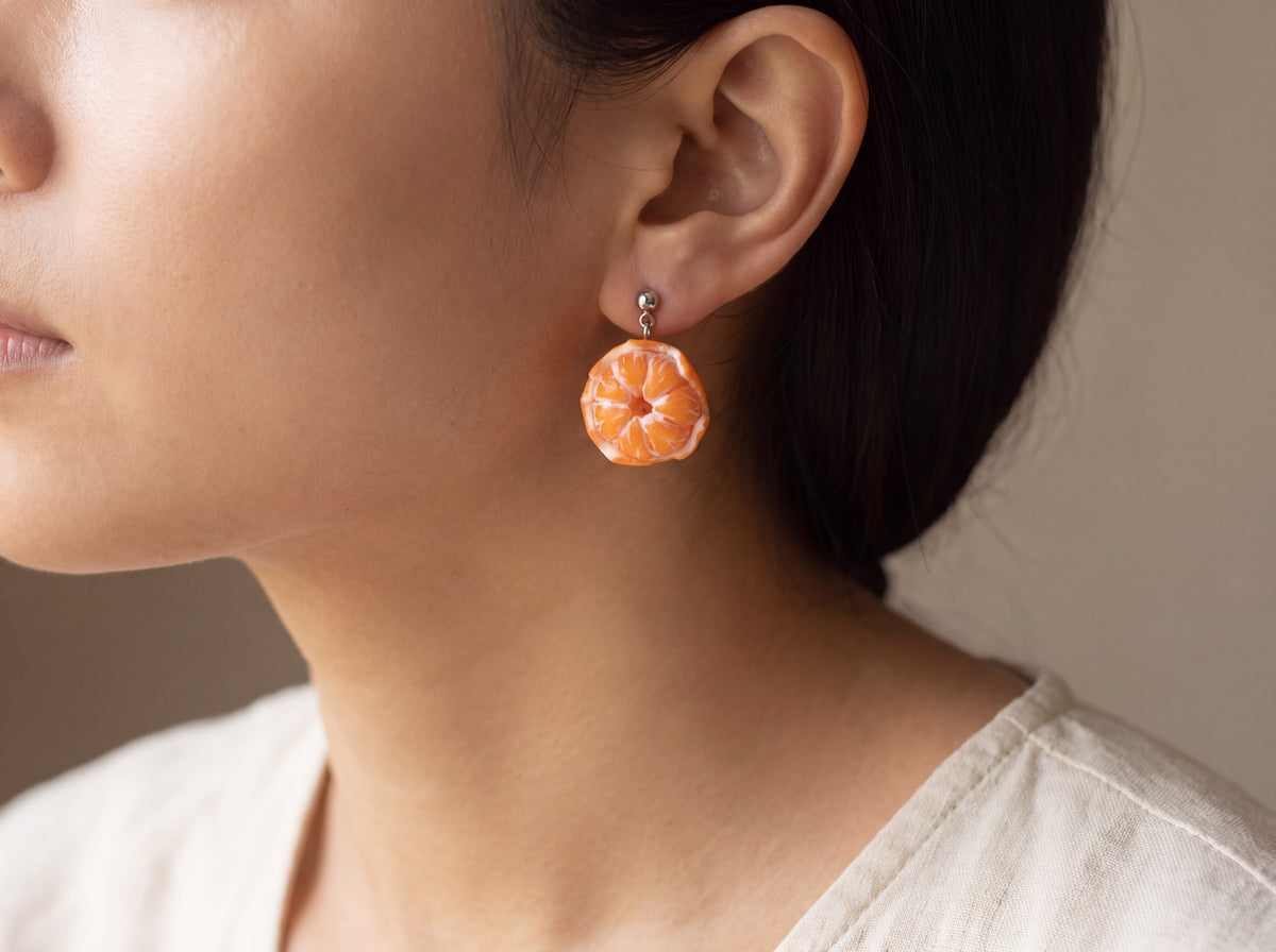 Handmade peeled tangerine earring with realistic orange segments and beaded rim, worn on a model's ear with a silver stud.
