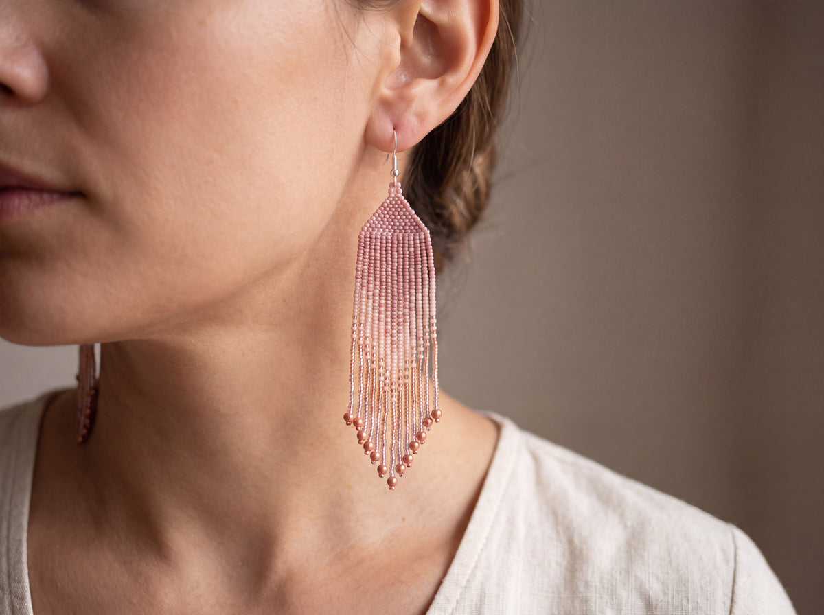 Long handmade beaded fringe earring in blush pink and rose gold ombre with copper bead tips, worn on a model