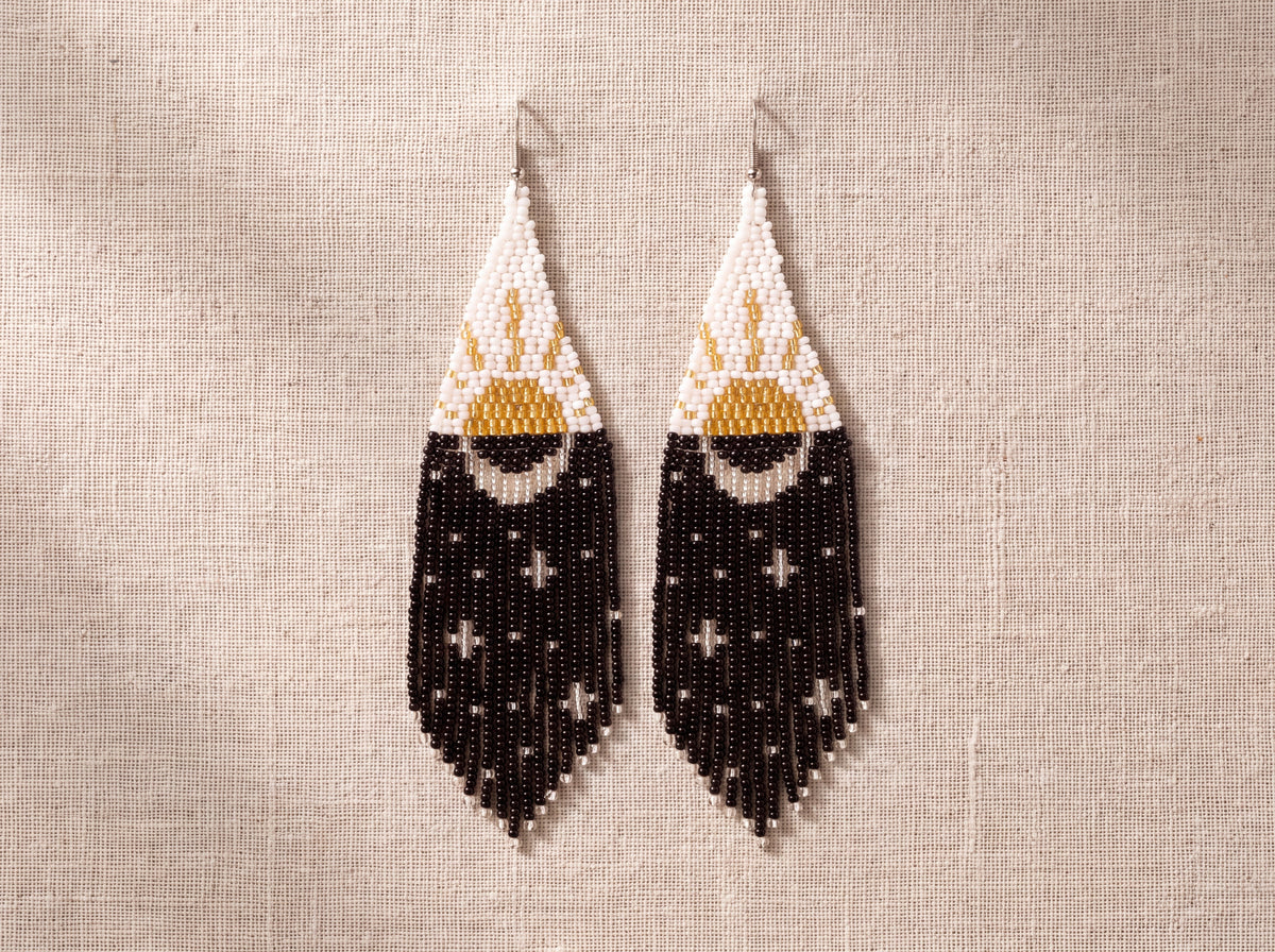 Pair of day and night beaded fringe earrings laid side by side on oatmeal linen