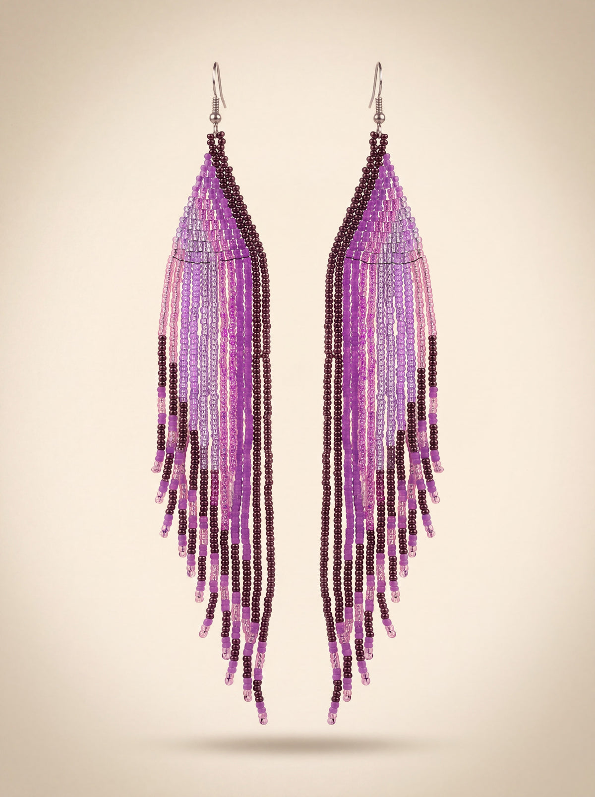 Extra long handmade beaded fringe earrings in purple, lilac and dark plum seed beads hanging side by side, on cream