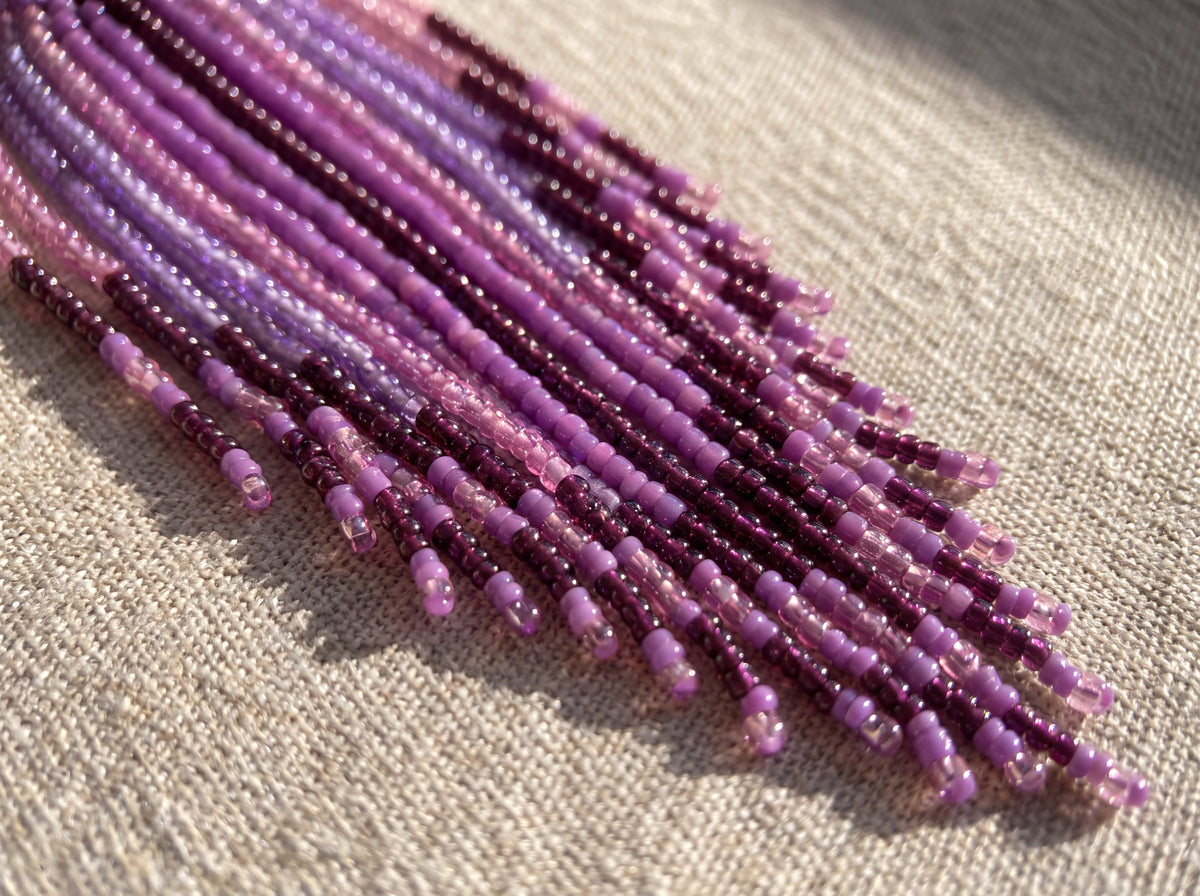 Macro detail of purple, lilac, pink and plum seed-bead fringe strands on oatmeal linen