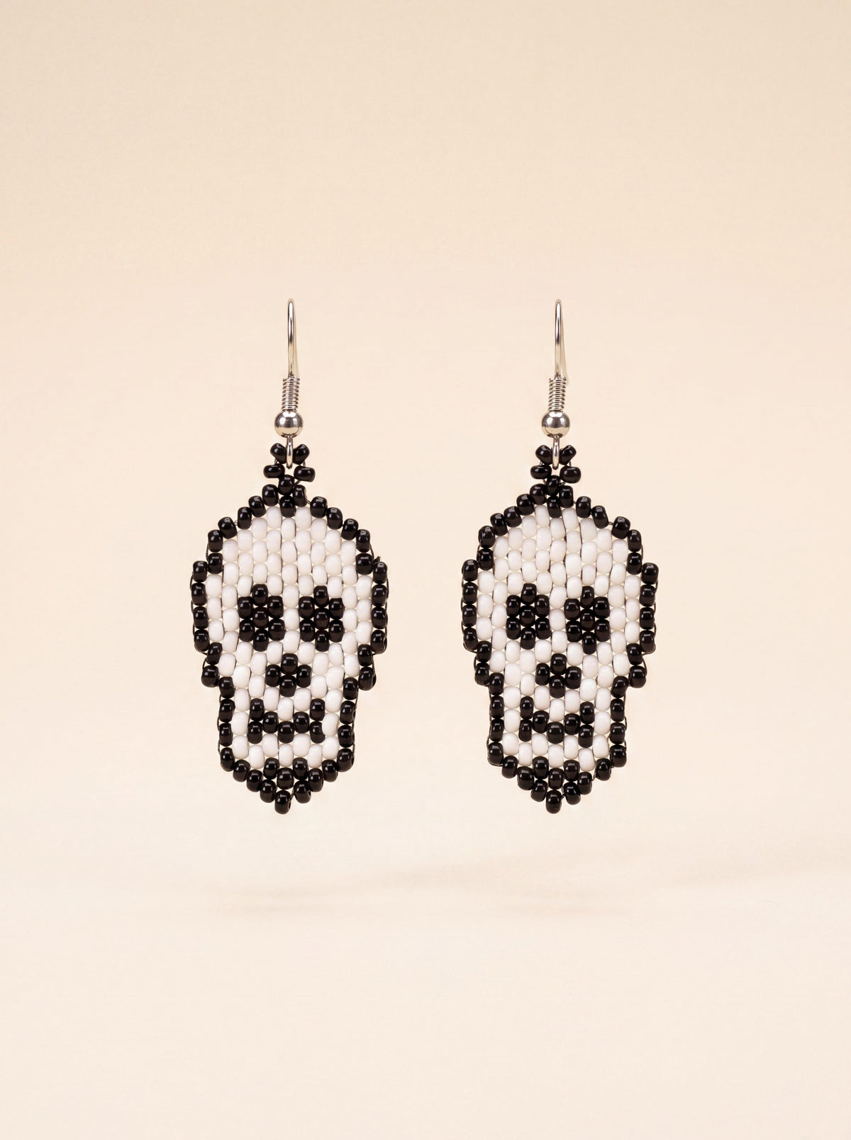 Pair of black and white beaded skull earrings on cream