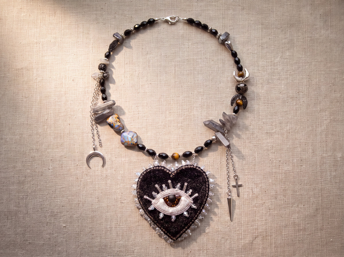 Black heart necklace laid flat from above showing the full strand, charms and heart pendant