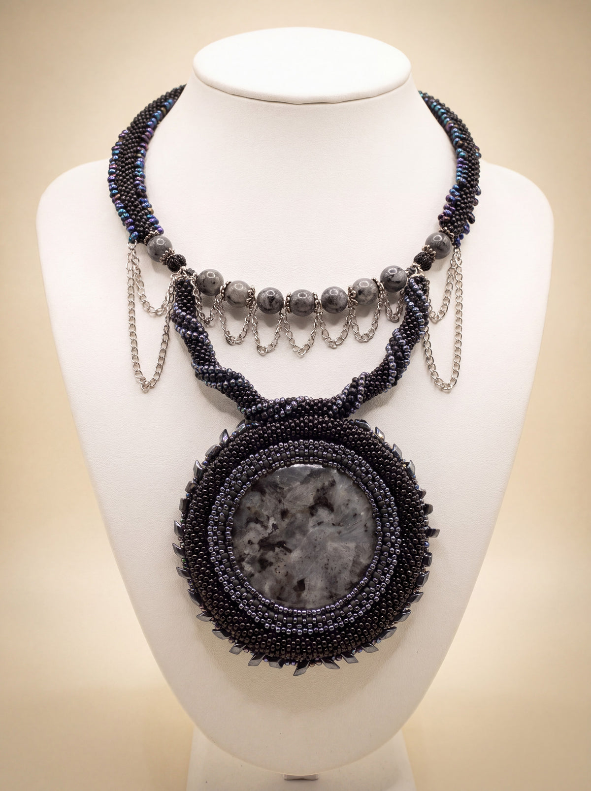 Handmade bead-crochet necklace "Black Moon" with larvikite stones, silver chains and a round stone medallion, on a white bust