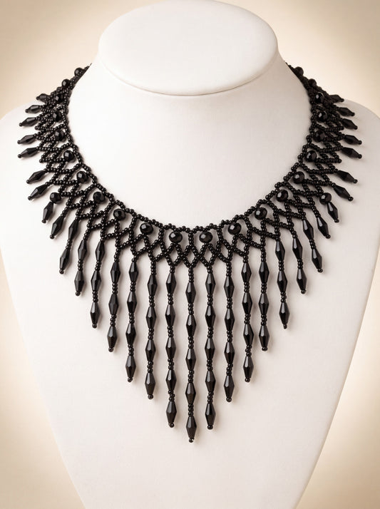 Handmade black beaded net collar with a fringe of long faceted black drops forming a V, on a white bust