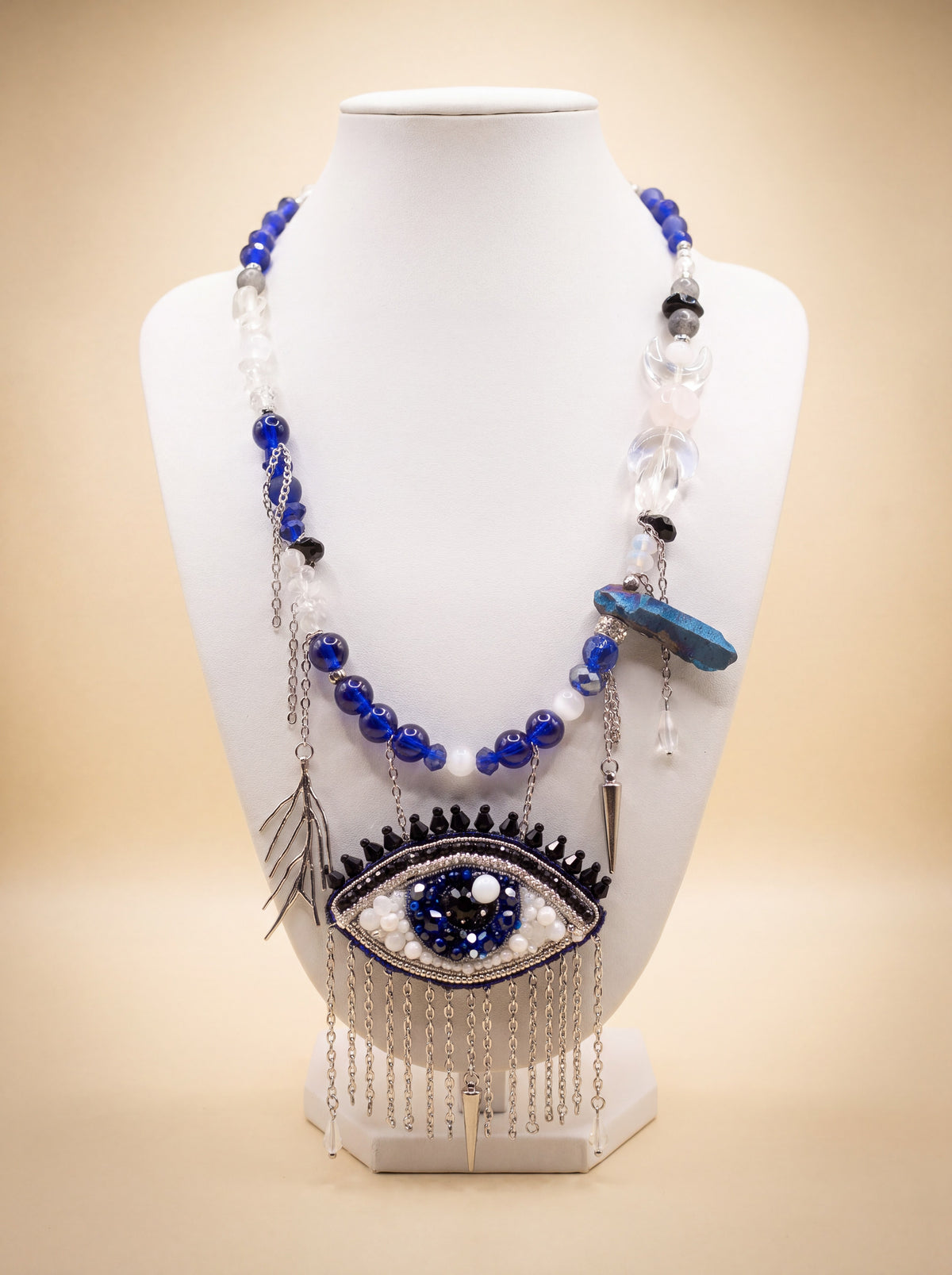 Handmade evil eye statement necklace with cobalt glass and stone beads, silver chains and bead-embroidered eye pendant with chain fringe, on a white bust