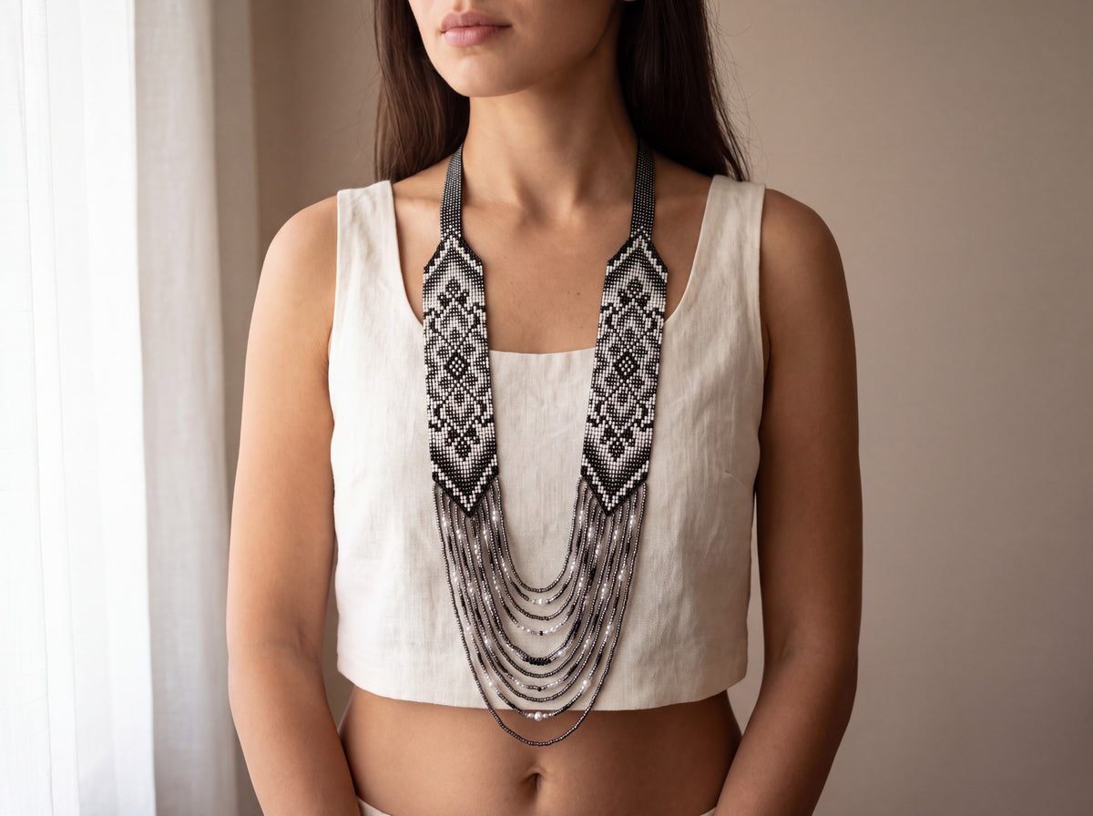 Model wearing a handmade black and white beaded gerdan necklace with ornamental strap pattern and layered graphite strands with pearls.