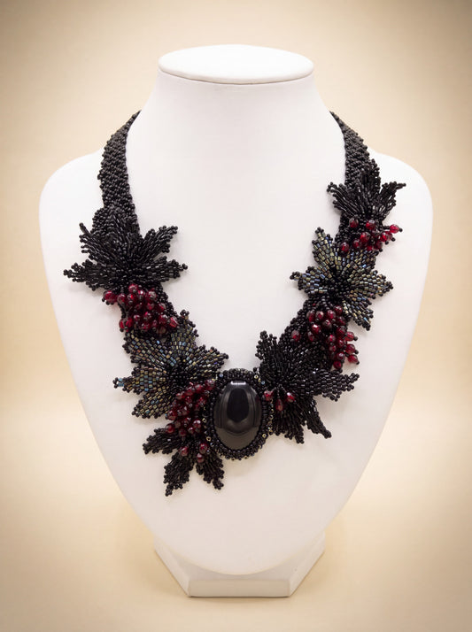 Handmade beaded statement collar with black leaves, red berries and an oval black natural stone cabochon, on a white bust