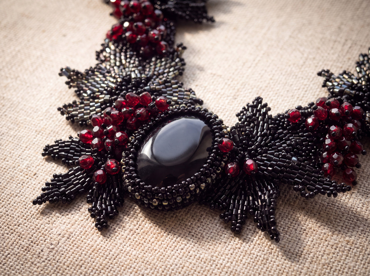Macro detail of the black natural stone cabochon in its beaded bezel with red berries and black leaves