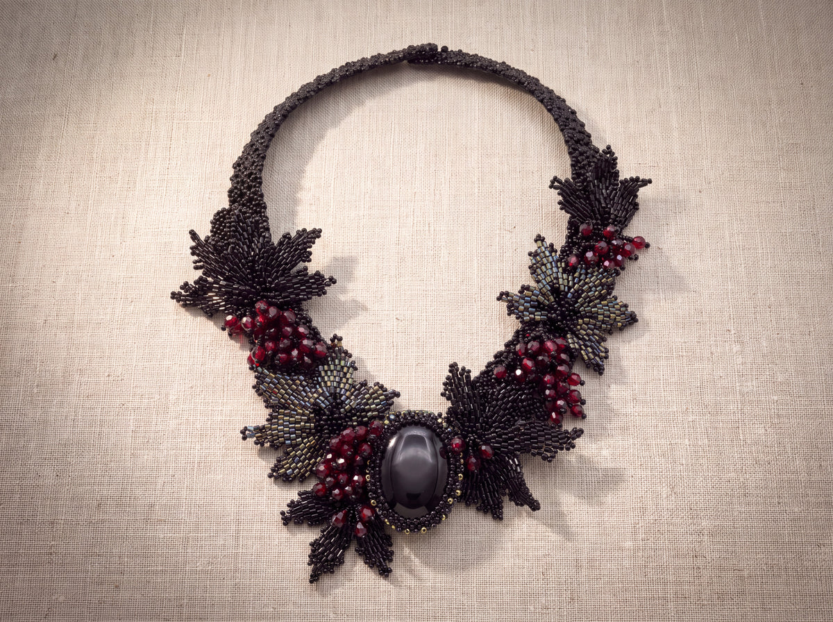 Black stone collar laid flat from above showing every beaded leaf and berry cluster