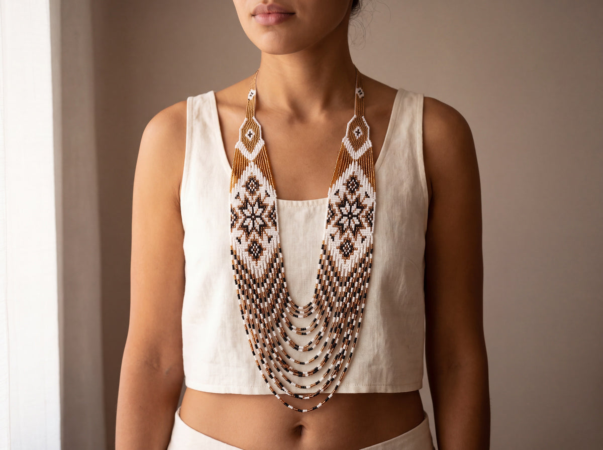 Handmade gold, white and black beaded gerdan necklace with star motifs and layered looping strands, worn over a cream linen top.