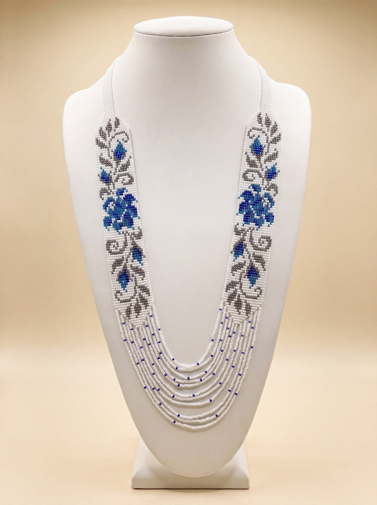 Handmade beaded necklace "Prolisok" with loomed blue floral pattern on white and beaded fringe strands.