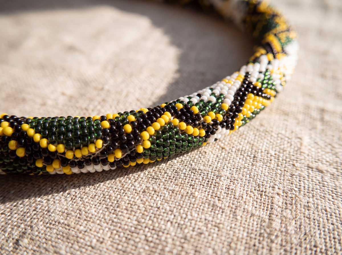 Close-up detail of a handmade bead-crochet necklace showing the snakeskin pattern of green, yellow, black and white seed beads on linen fabric