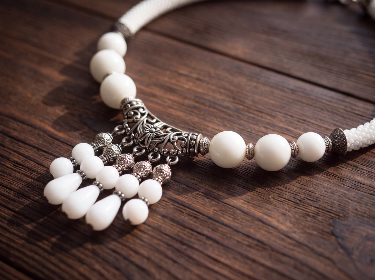 Close-up of a handmade white bead necklace on dark wood, showing the silver filigree centerpiece with white teardrop dangles and beaded rope