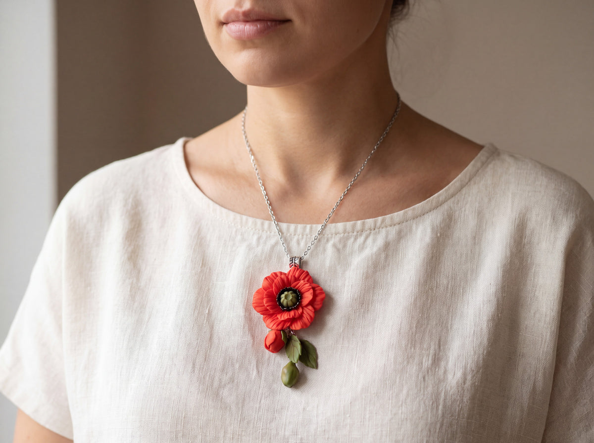 Handmade red poppy pendant with bud and green leaves on a silver chain, worn by a model in a cream linen top.
